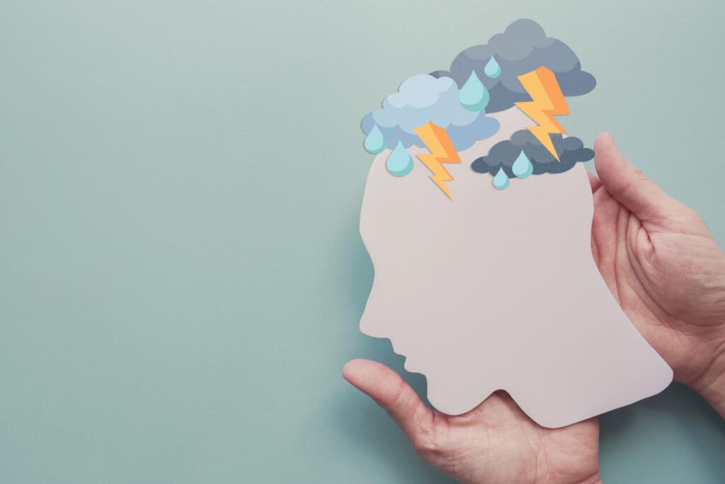 A paper cut-out head with storm clouds laid over it