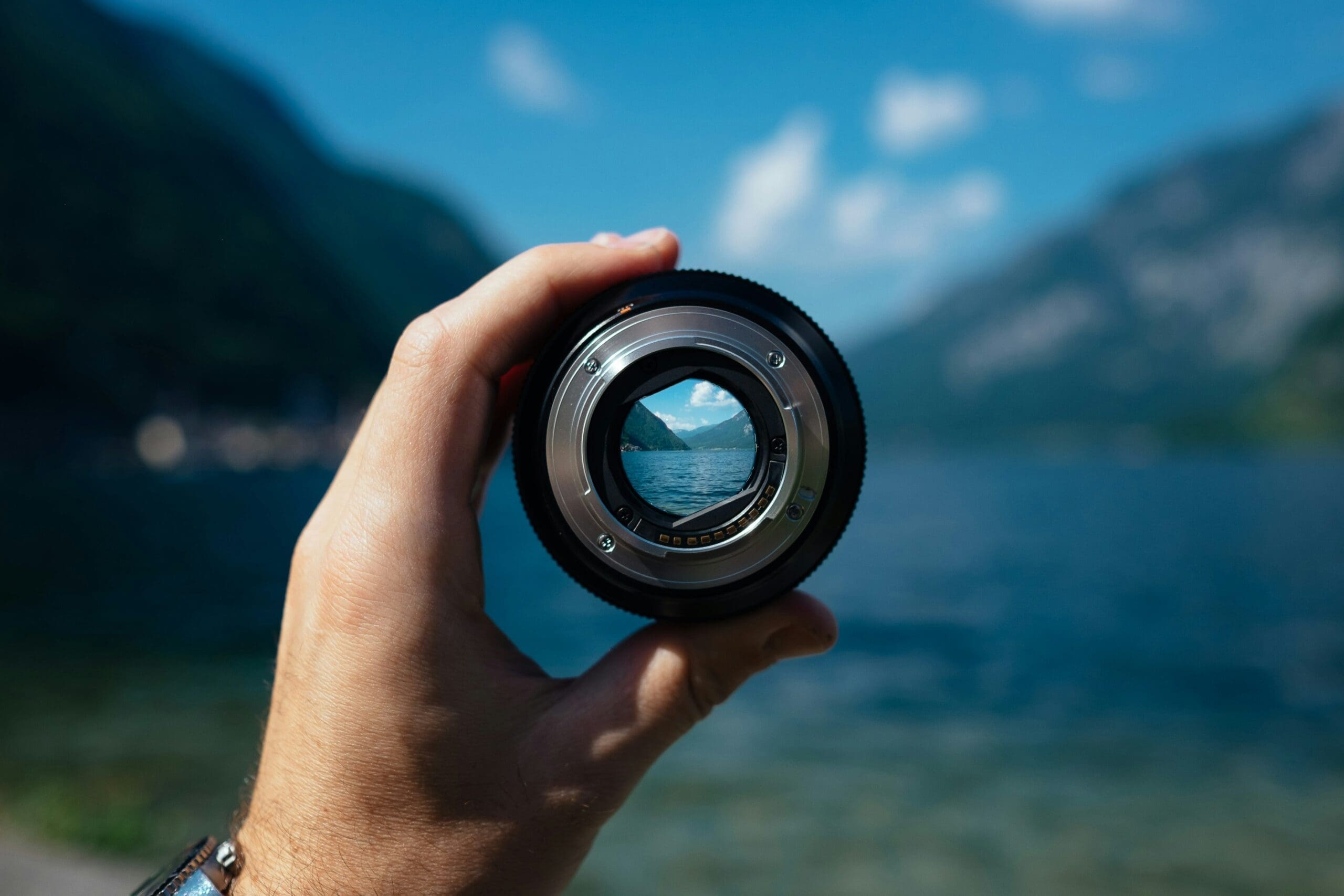 a hand holding a lense in front of a body of water to represent monotropism, focus, and the monotropic processing style